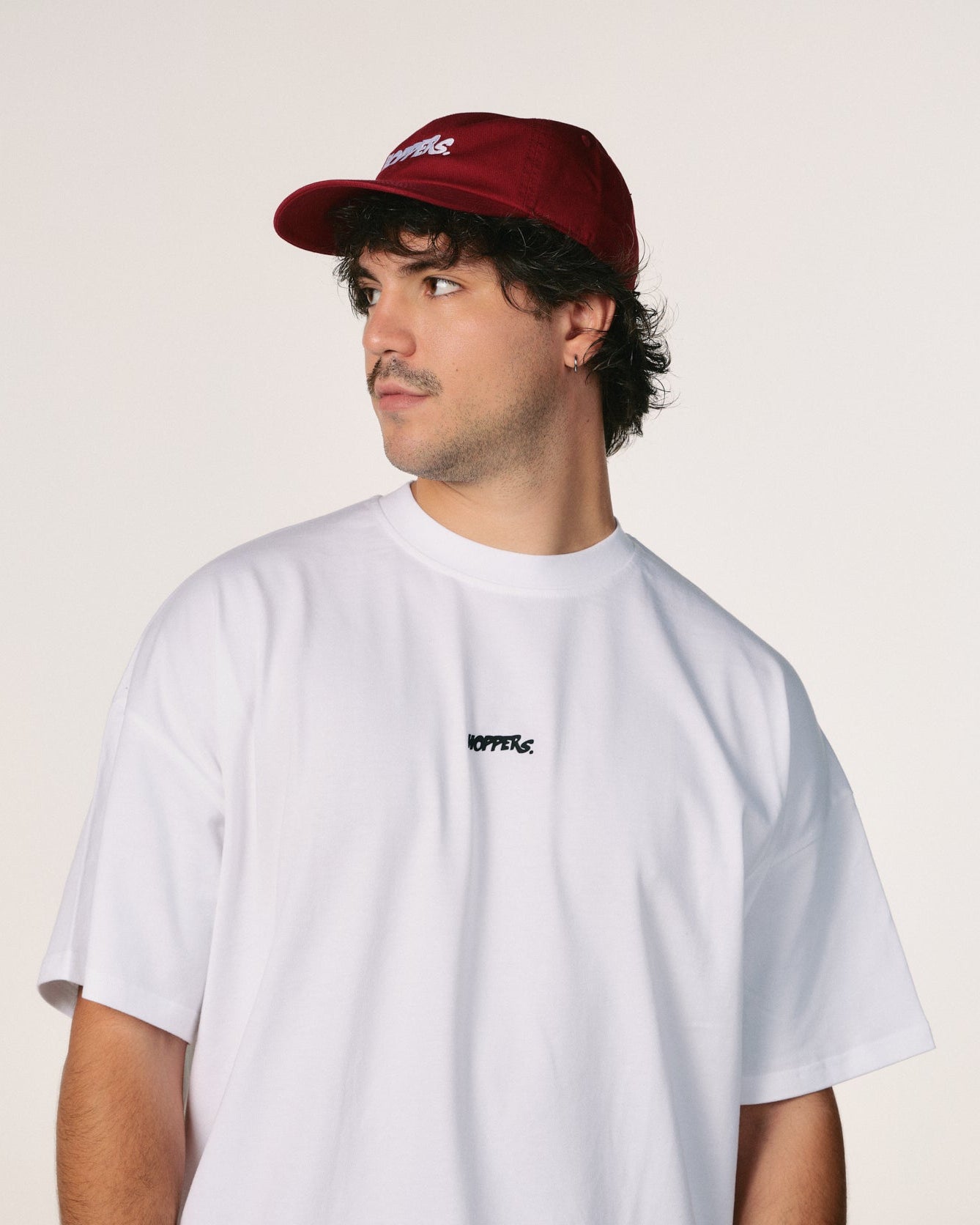 Person wearing a white t-shirt with a logo and a red cap on a plain background