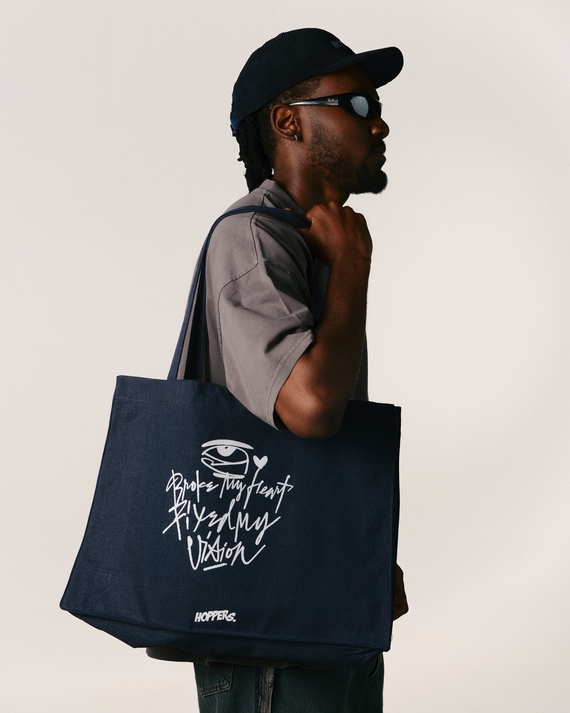 Man holding a navy tote bag with text and logo on a plain background