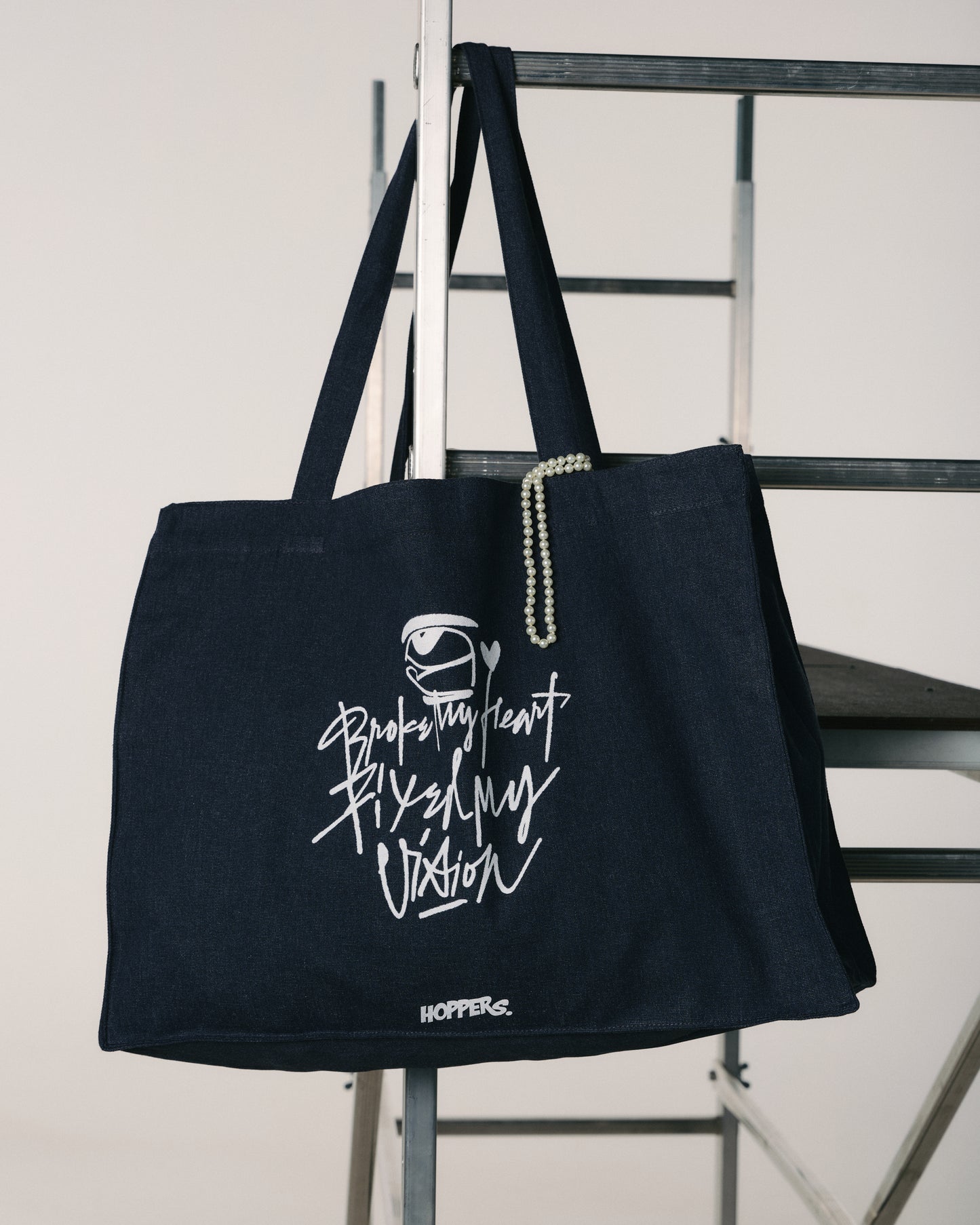 Black tote bag with white text and logo on a metal chair against a white background