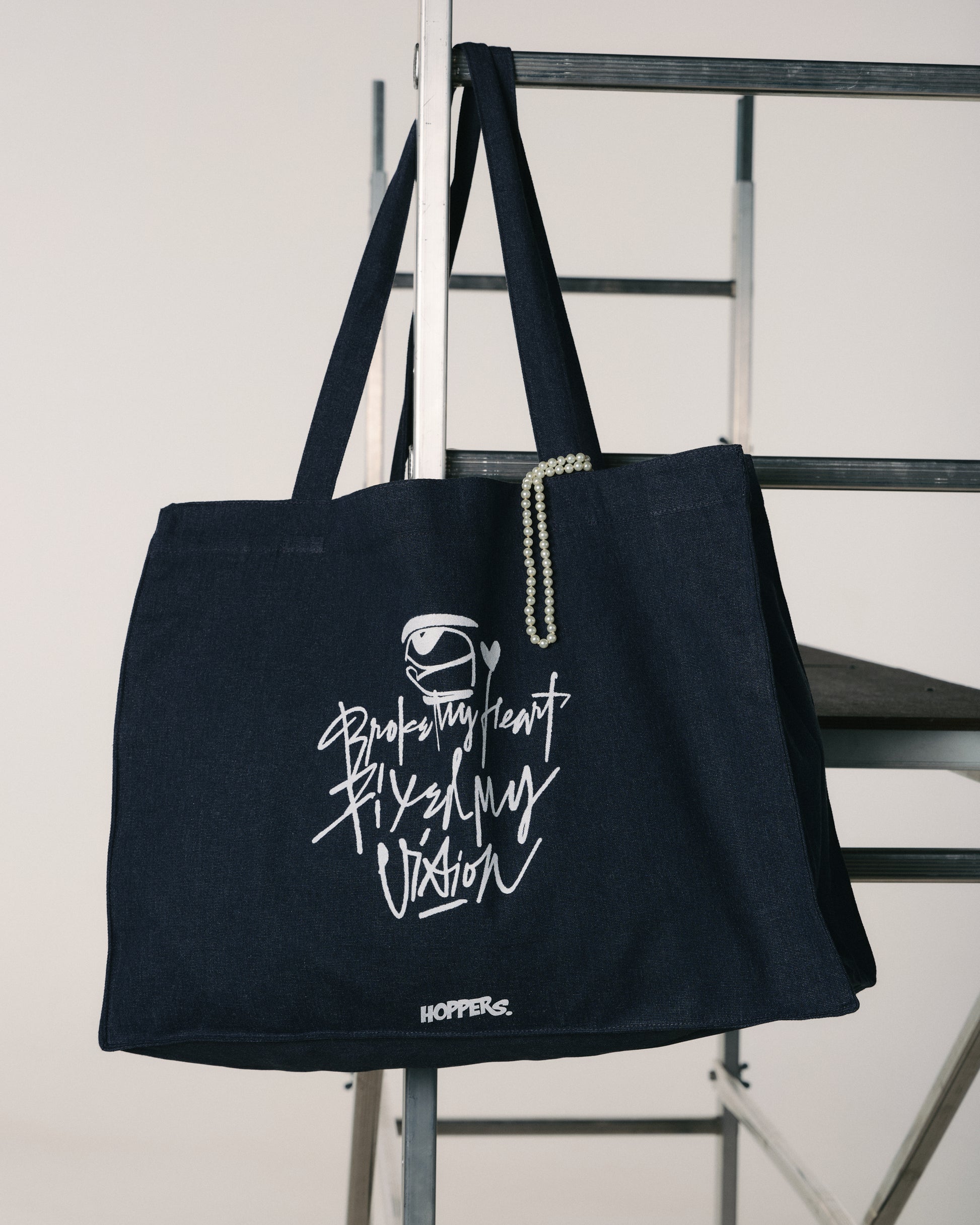 Black tote bag with white text and logo on a metal chair against a white background