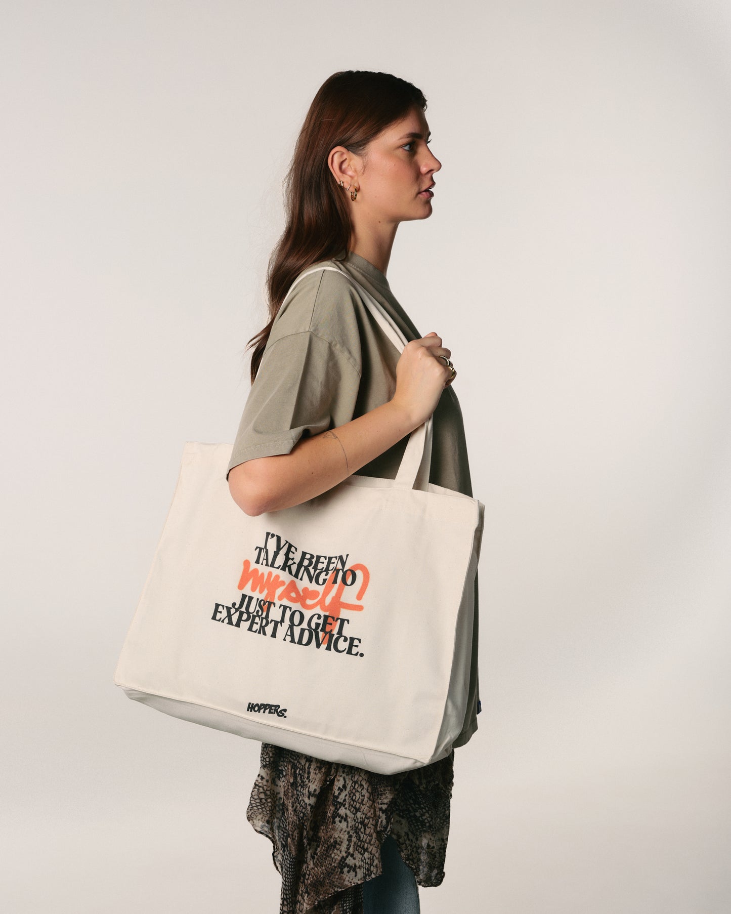 Woman holding a tote bag with text  "I've been talking to myself" on a plain background
