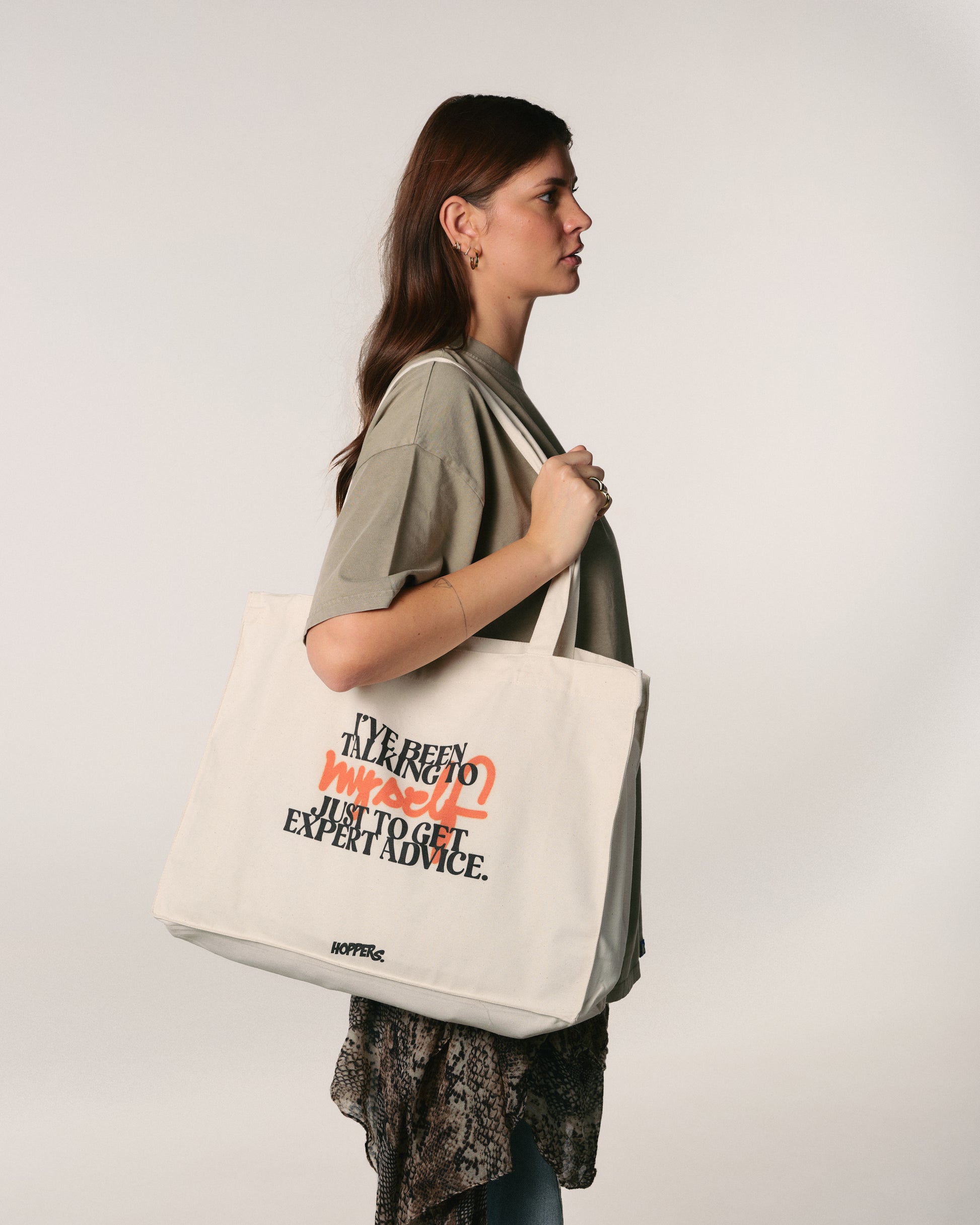 Woman holding a tote bag with text  "I've been talking to myself" on a plain background