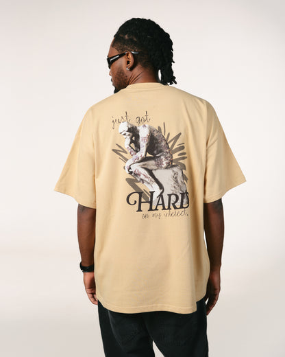 Man with braided hair and sunglasses wearing a beige Hoppers Hip Hop Takeovers T-shirt. The shirt features a graphic of a contemplative statue with the text, "just got HARD on my intellect."