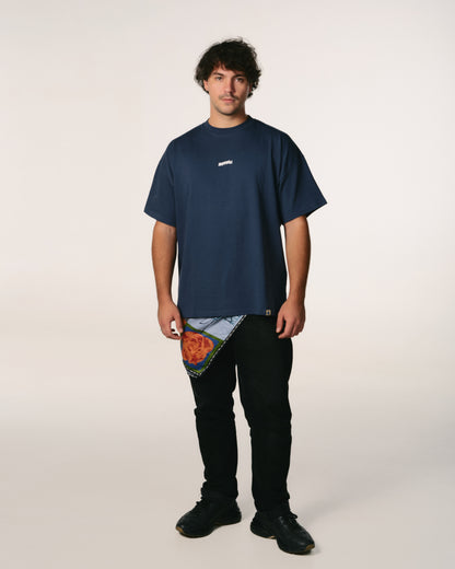 A man stands against a plain background wearing a loose navy  Hoppers Hip Hop Takeovers T-shirt and black pants. His expression is neutral. The mood appears casual and relaxed.