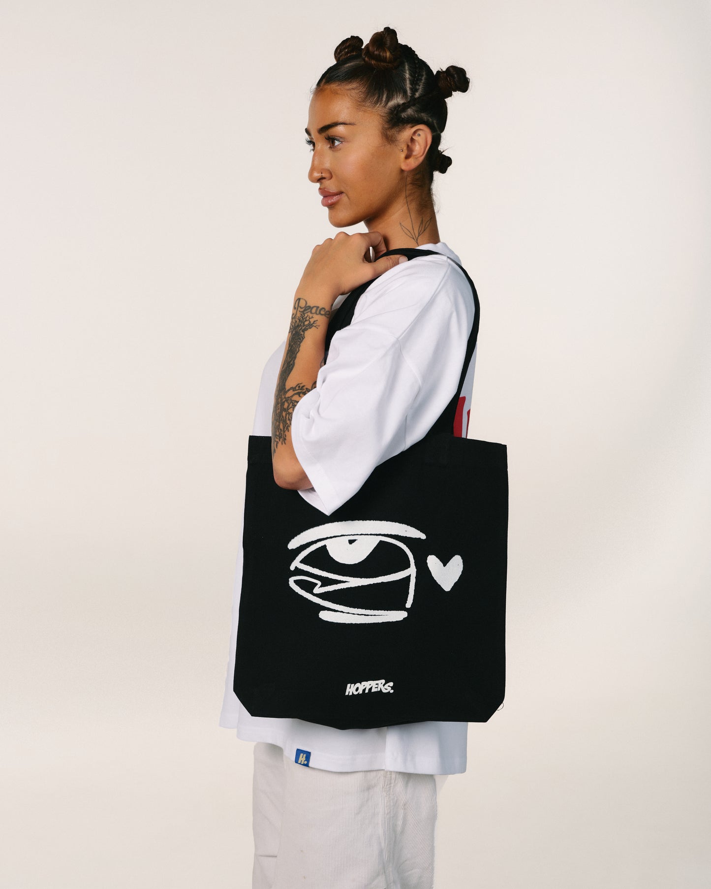 Person holding a black tote bag with a white logo and text on a plain background