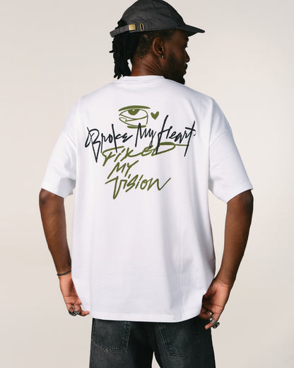 Person wearing a white hoppers hip hop takeovers t-shirt with text broke my heart fixed my vision and an eye design on the back, standing against a plain background Tricou oversized unisex Broke My Heart alb hip hop takeovers hoppers