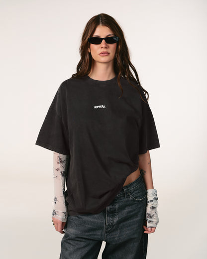 Person wearing a black oversized t-shirt with a brand logo, sunglasses, and tattoos on arms and hands against a white background. Tricou oversized unisex Hoppers Talking to Myself vintage grey, vedere frontala pe model, hip hop takeovers
